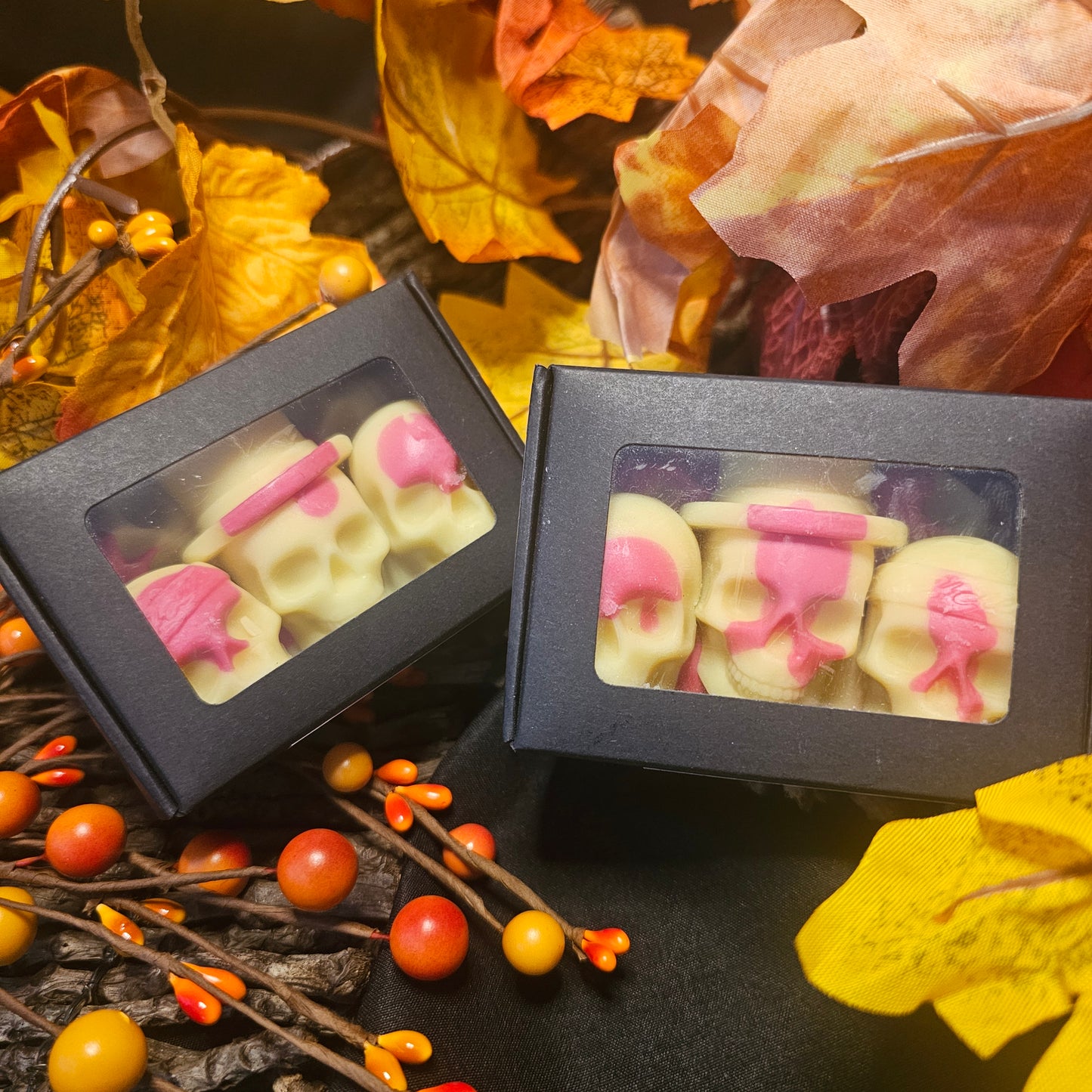 Two boxes of fireside skull shaped wax melts against a dark background filled with autumn colours, dried leaves and berries