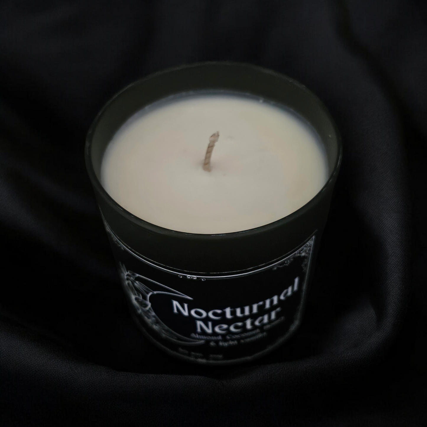 A Candle in a black container on a midnight blue fabric background