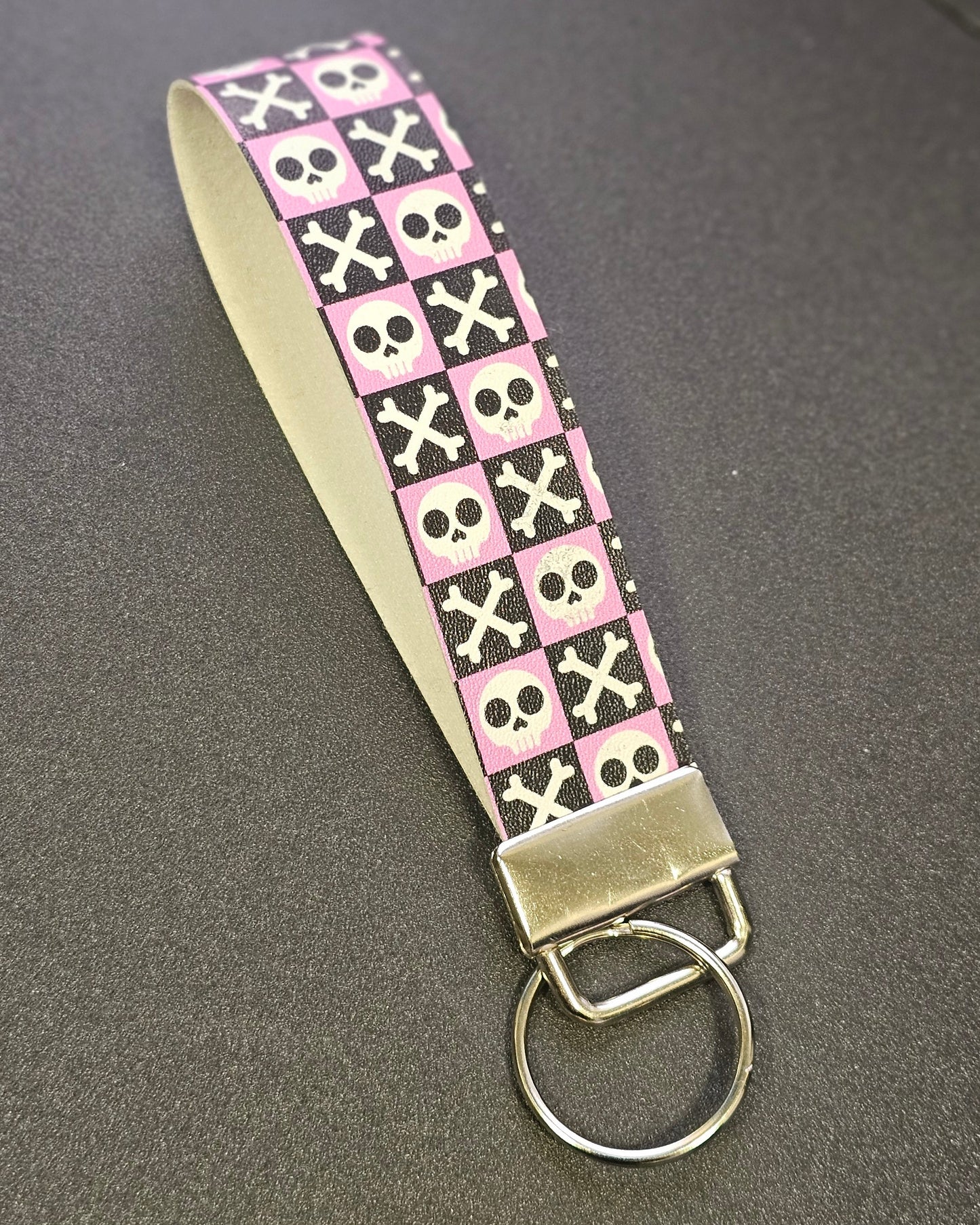Keychain / Key Fob with pink and black pattern of skulls and crossbones on a grey surface