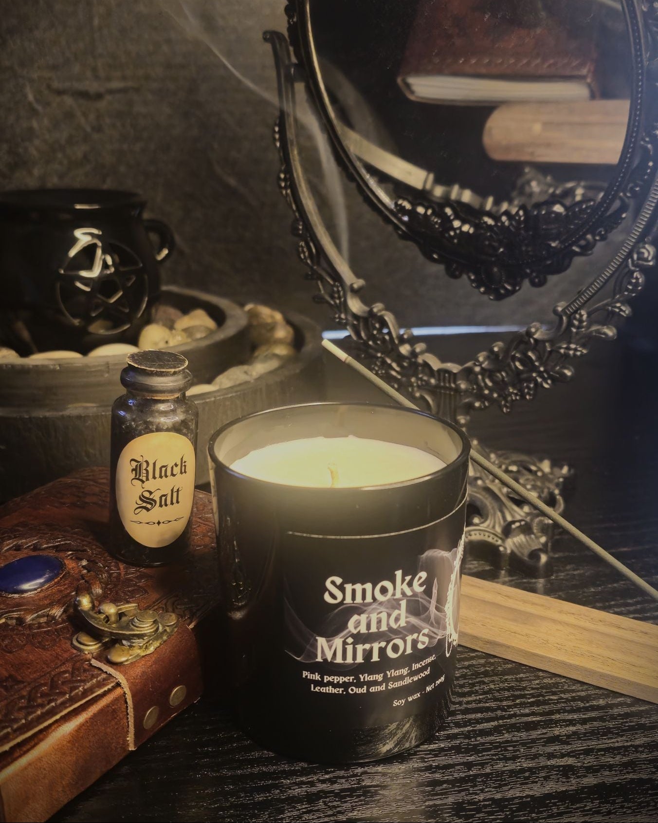 Candle labeled 'Smoke and Mirrors' with a bottle of 'Black Salt' on a dark acedemia themed background