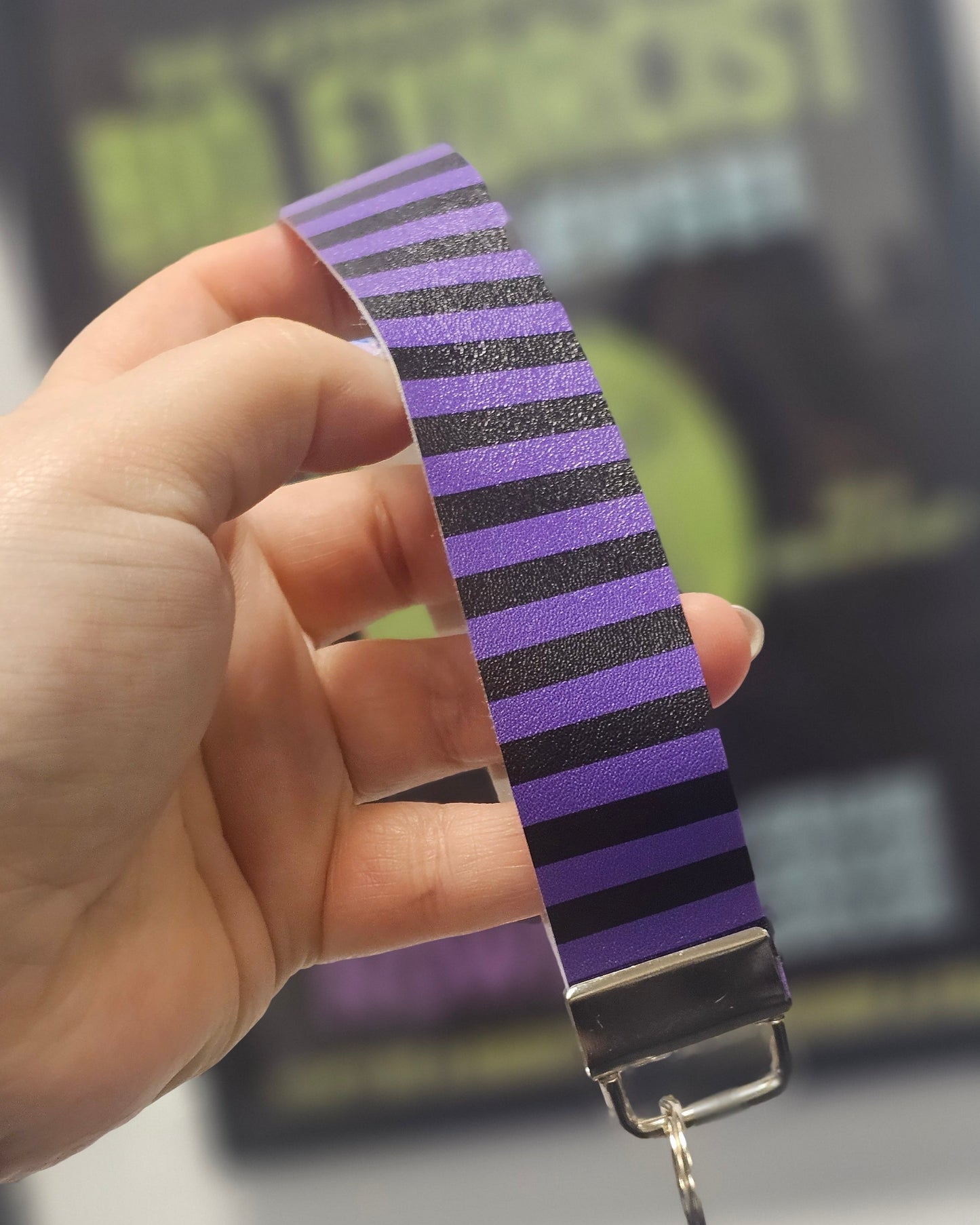 Hand holding a striped purple and black wrist strap / keyring with a blurred background