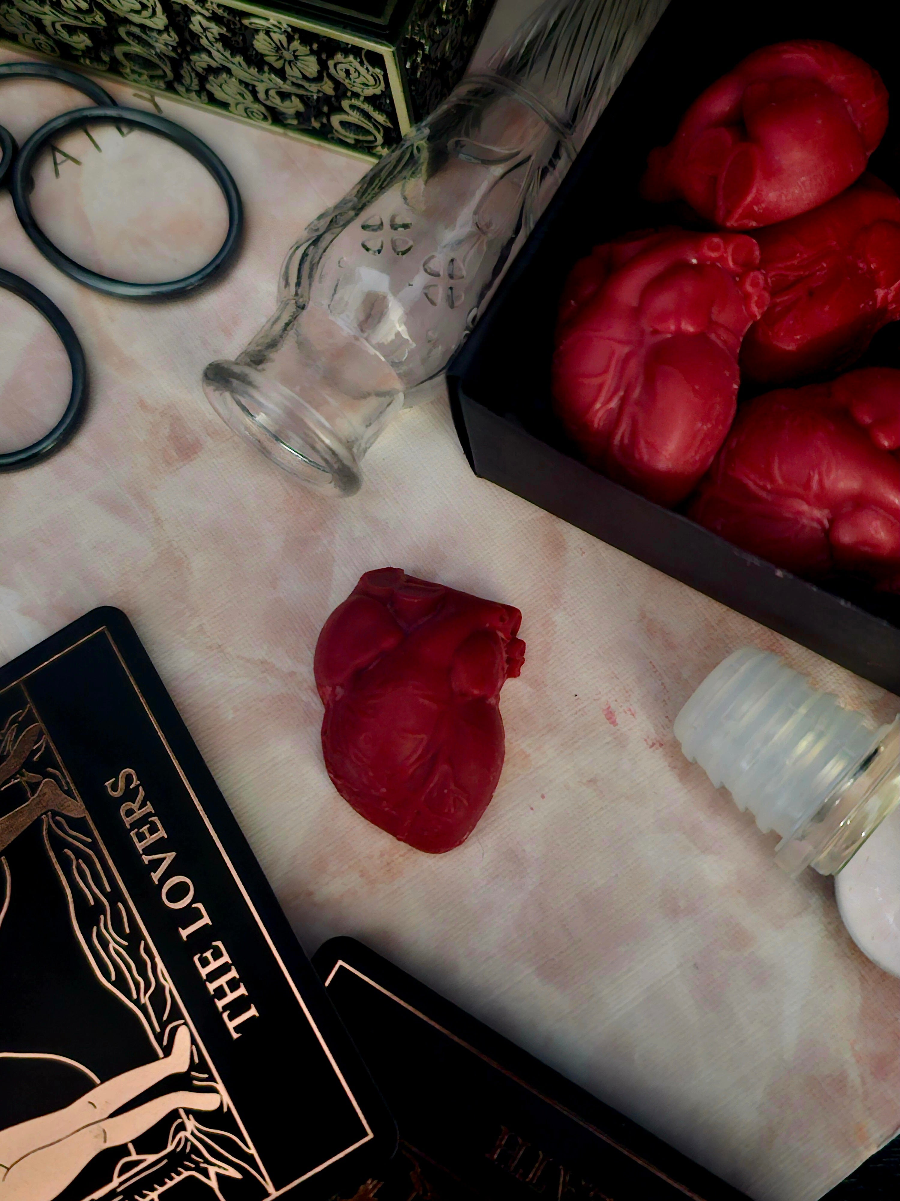Red heart-shaped wax melt, "the lovers" tarot card, and other items on a textured surface