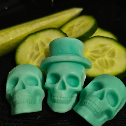 Close up image of 3 green skull shaped wax melts laying on a dark background with cucumber slices 
