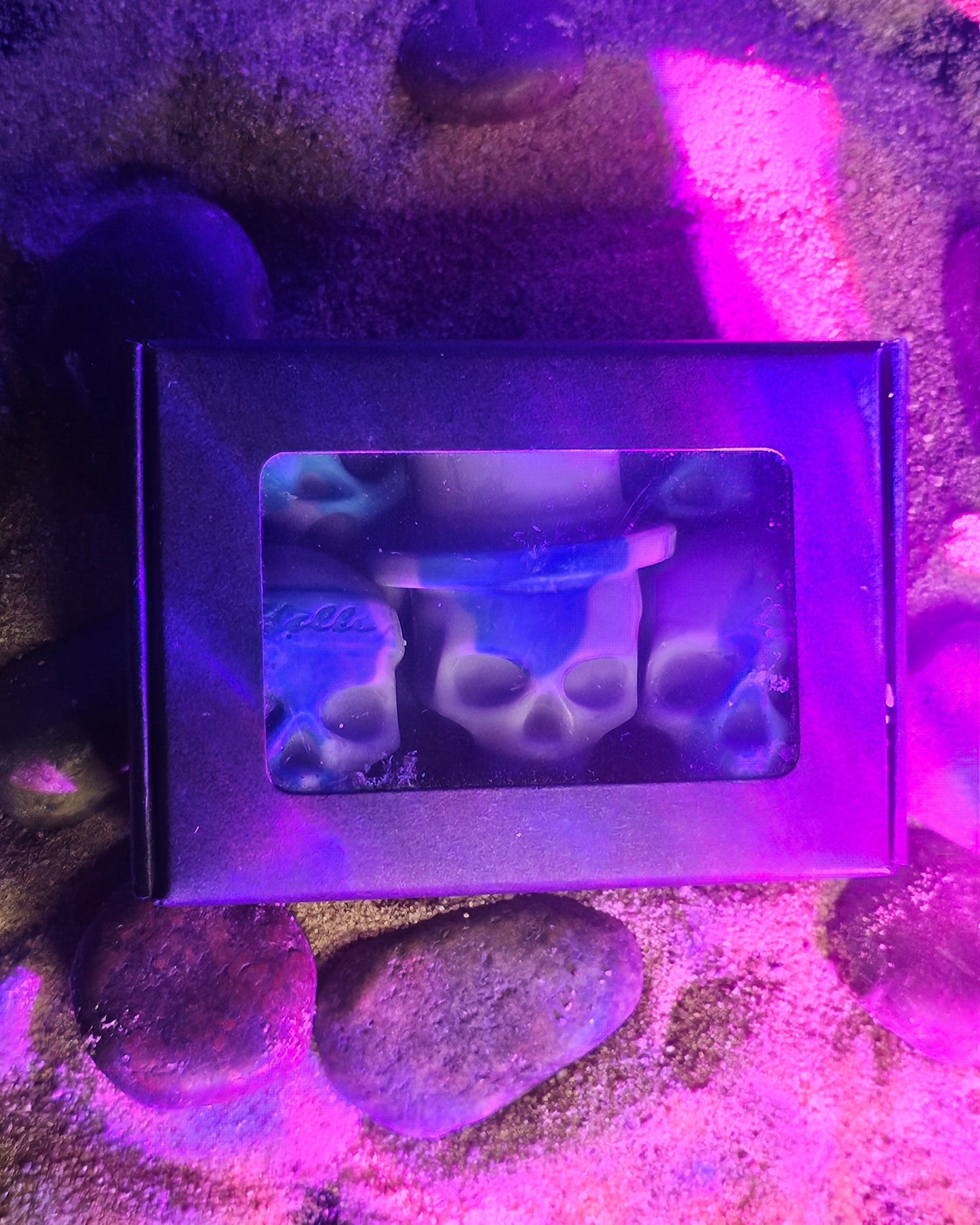 Product packaging with a clear window on a purple and pink sandy surface