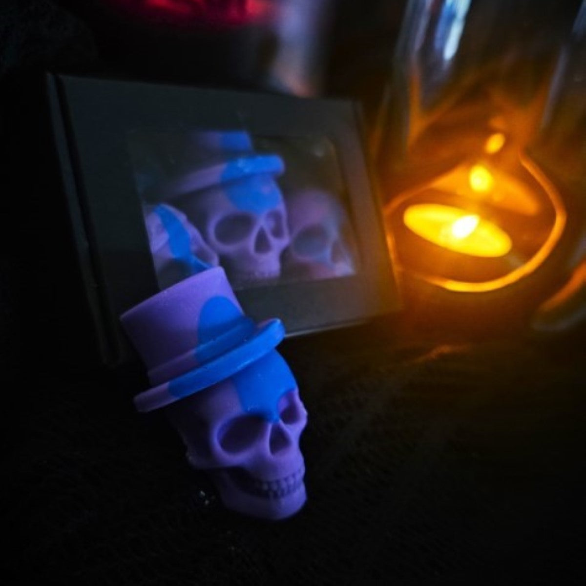 A skull-shaped wax melt illuminated by a light, with a blurred background featuring a box of the product  and candle.