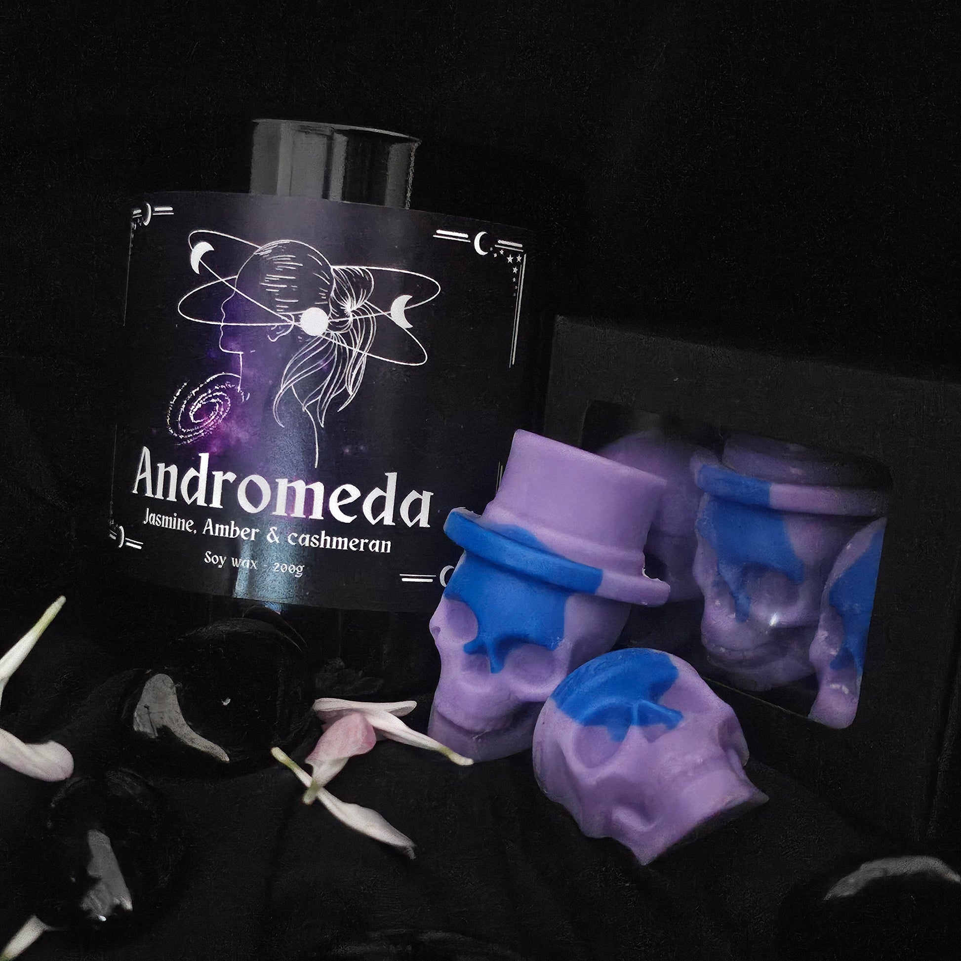 skull shaped wax melts and a black glass candle, labeled andromeda on a dark background 