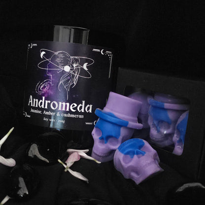 skull shaped wax melts and a black glass candle, labeled andromeda on a dark background 
