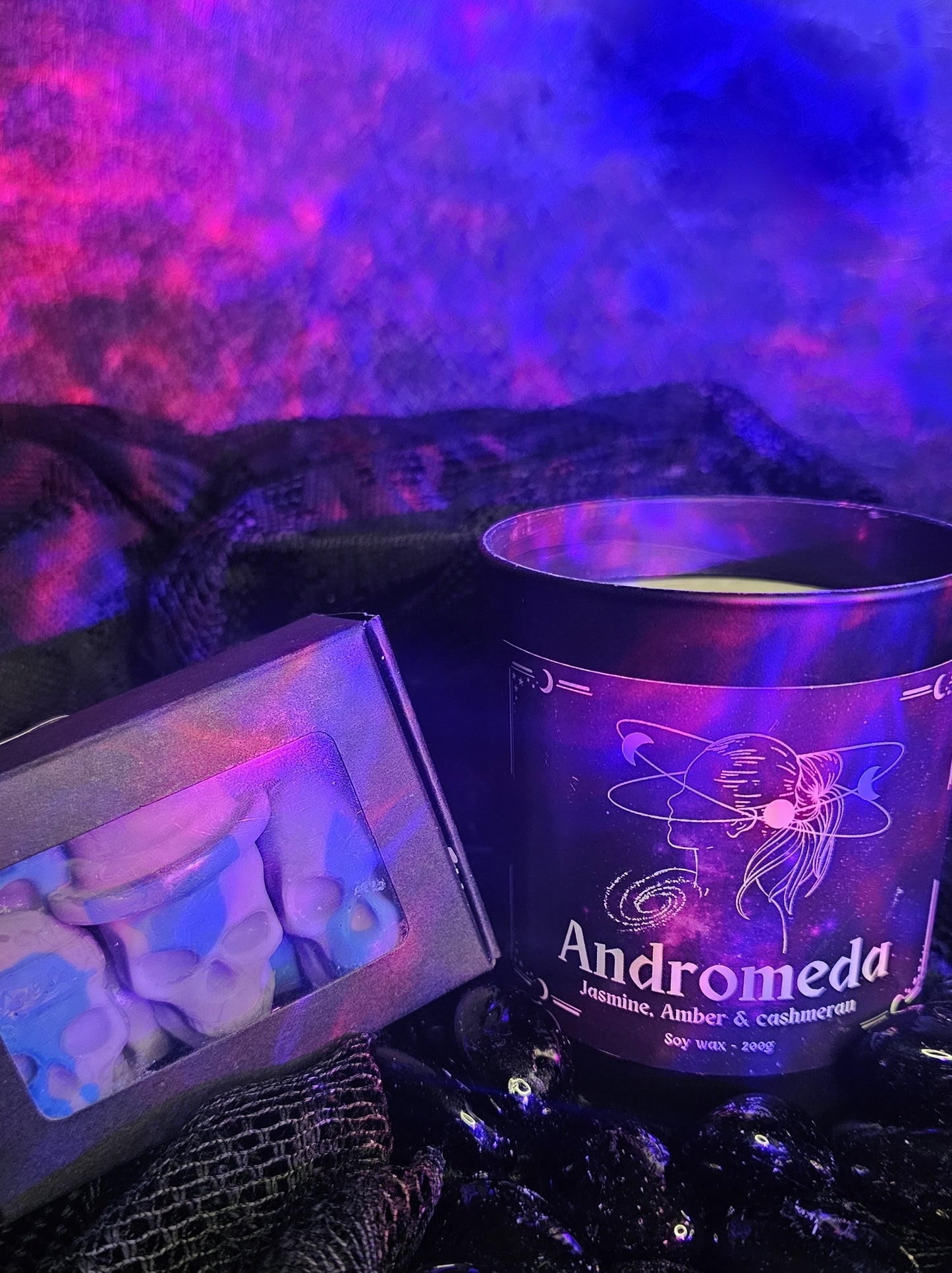 Candle labeled 'Andromeda' with decorative packaging on a dark background