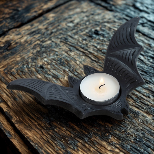 Black bat-shaped candle holder with a lit white candle on a wooden surface