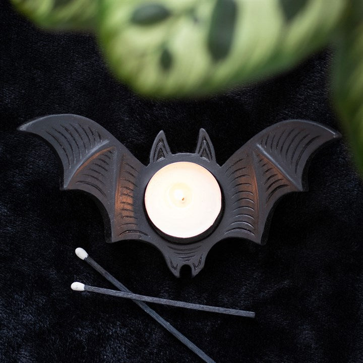 Bat-shaped candle holder with a lit candle on a dark surface