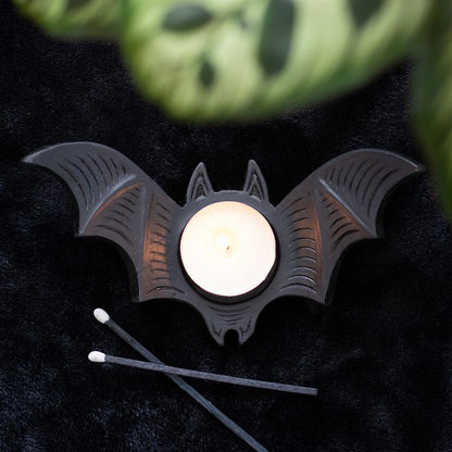 Bat-shaped candle holder with a lit candle on a dark surface