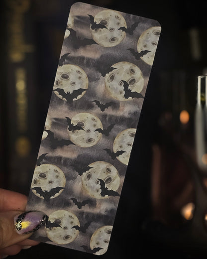 Bookmark with moon and bat pattern held by a hand against a dark candle lit background
