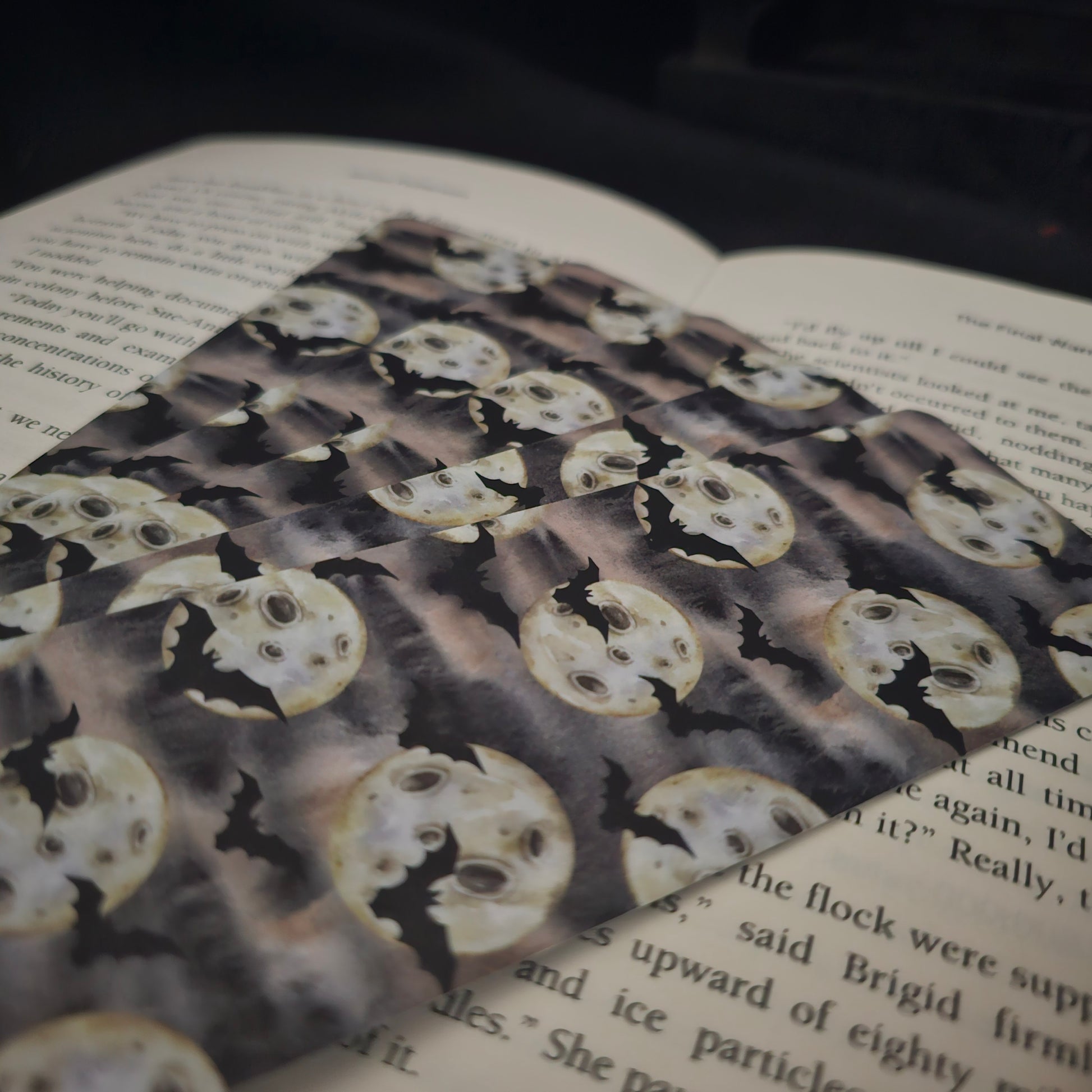 A pile of bookmarks with a bat and moon repeting pattern laying on an open book 