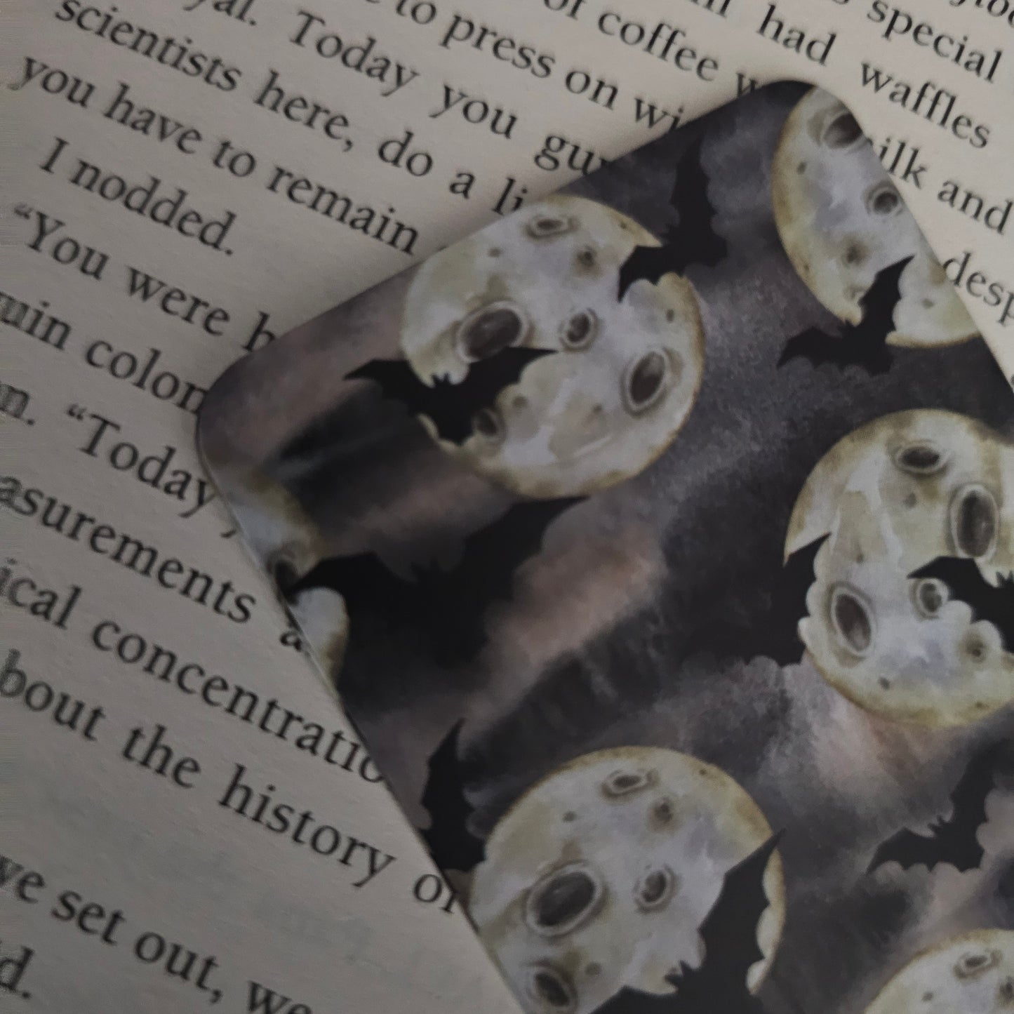 A bookmark with an illustration of bats flying around a moon, placed on an open book.