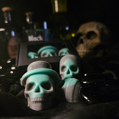 A set of skull-shaped wax melts, with a focus on their unique design featuring different shades of gray and teal.