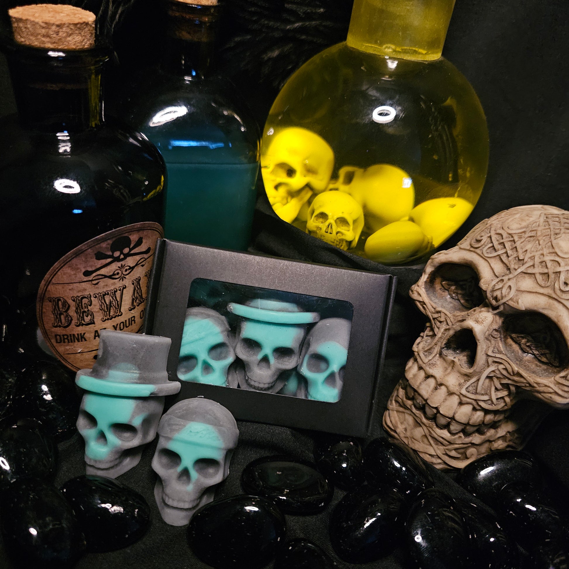 Several skull shaped wax melts, On a dark background with various alchemist style bottles and a skull covered in Celtic knot design 