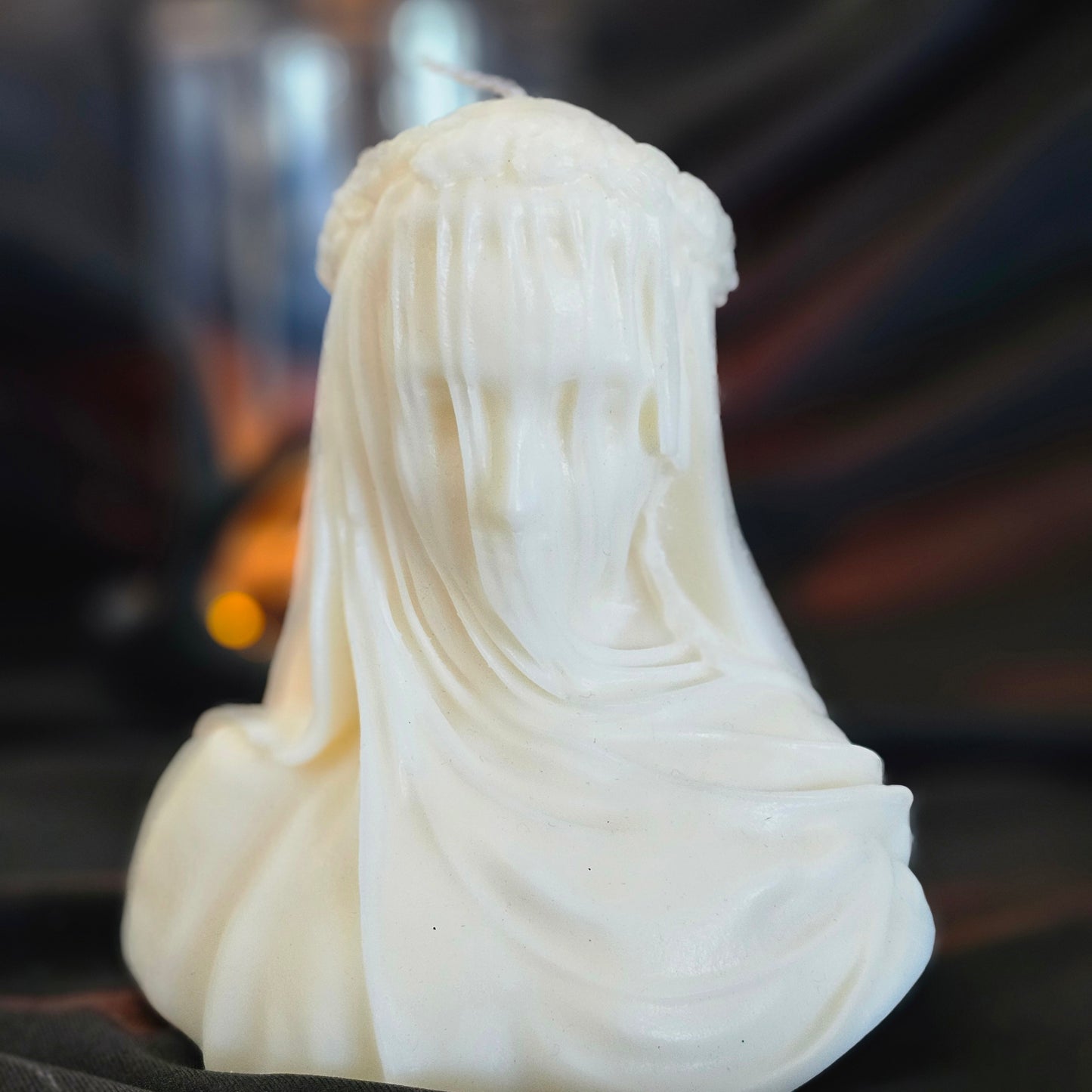 Off-white candle designed to resemble figure with a veil, with a smaller lit candle in the background creating a warm glow.