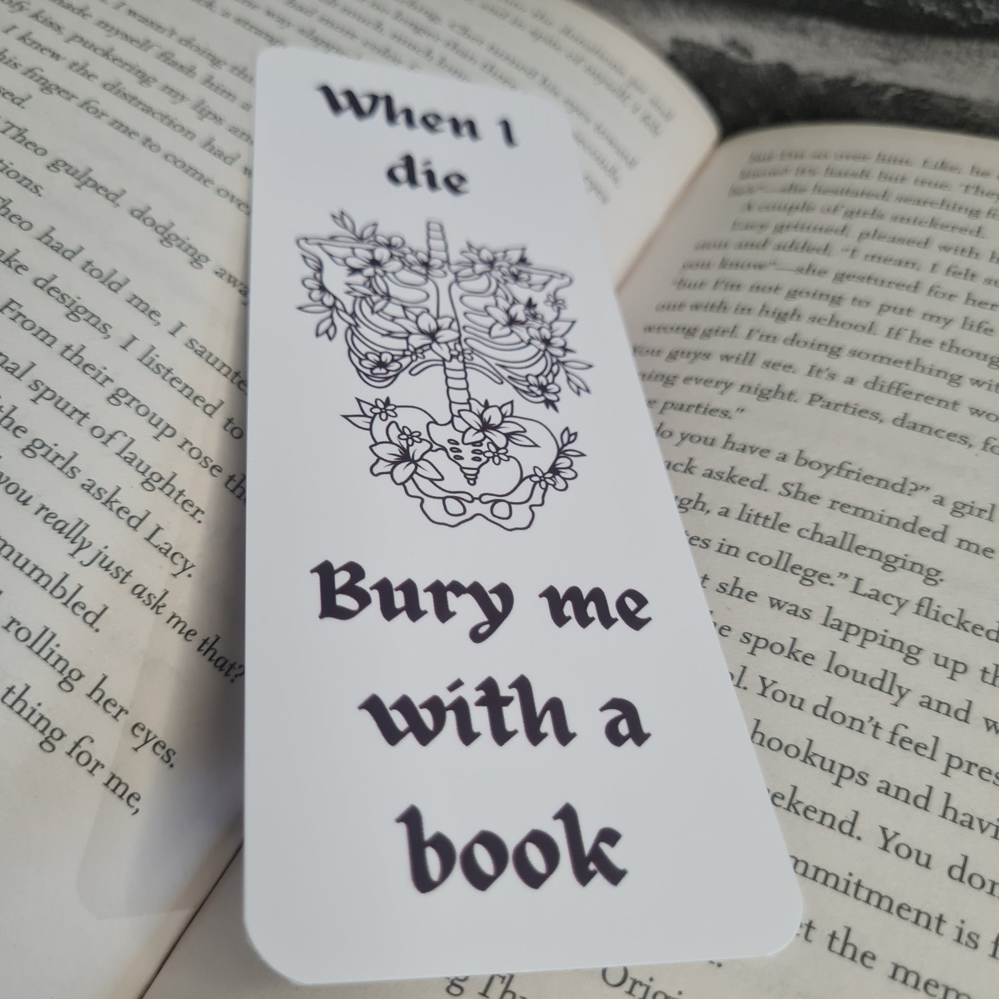 Bookmark with skeleton and floral design, text 'When I die, bury me with a book', on an open book 