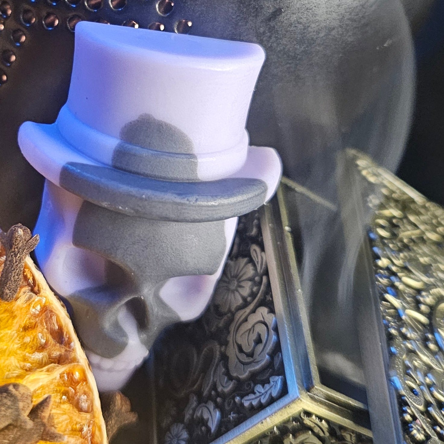 Wax melt skull with a top hat on a dark, ornate surface