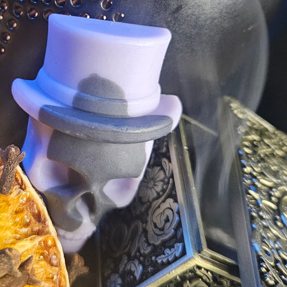 Wax melt skull with a top hat on a dark, ornate surface
