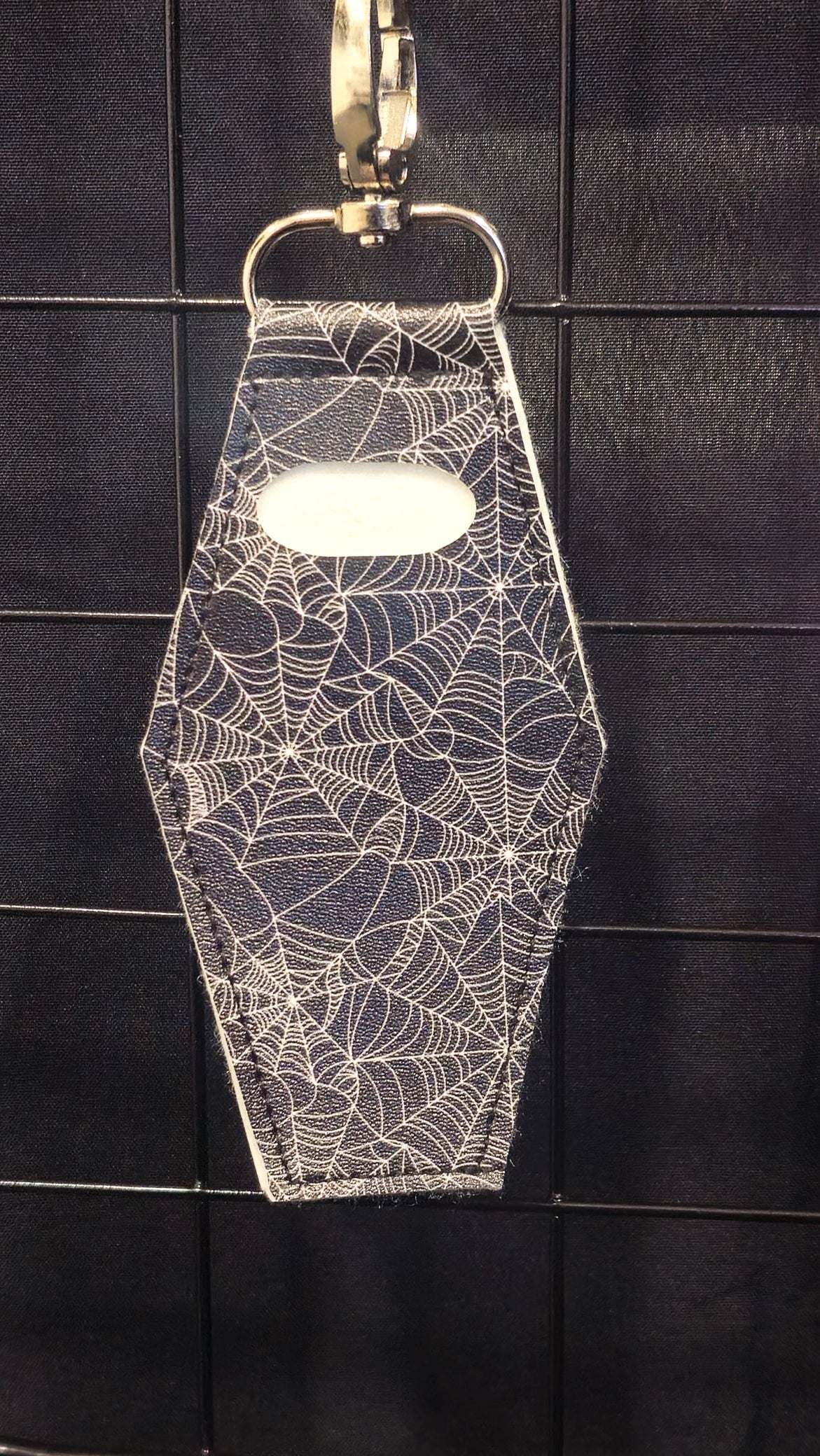 Coffin-shaped lip gloss holder keychain in black spiderweb print leatherette with stainless steel lobster clasp.