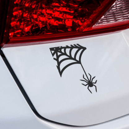 A black vinyl decal of a spider web with a spider on it, applied on the white surface of a vehicle's tail light.