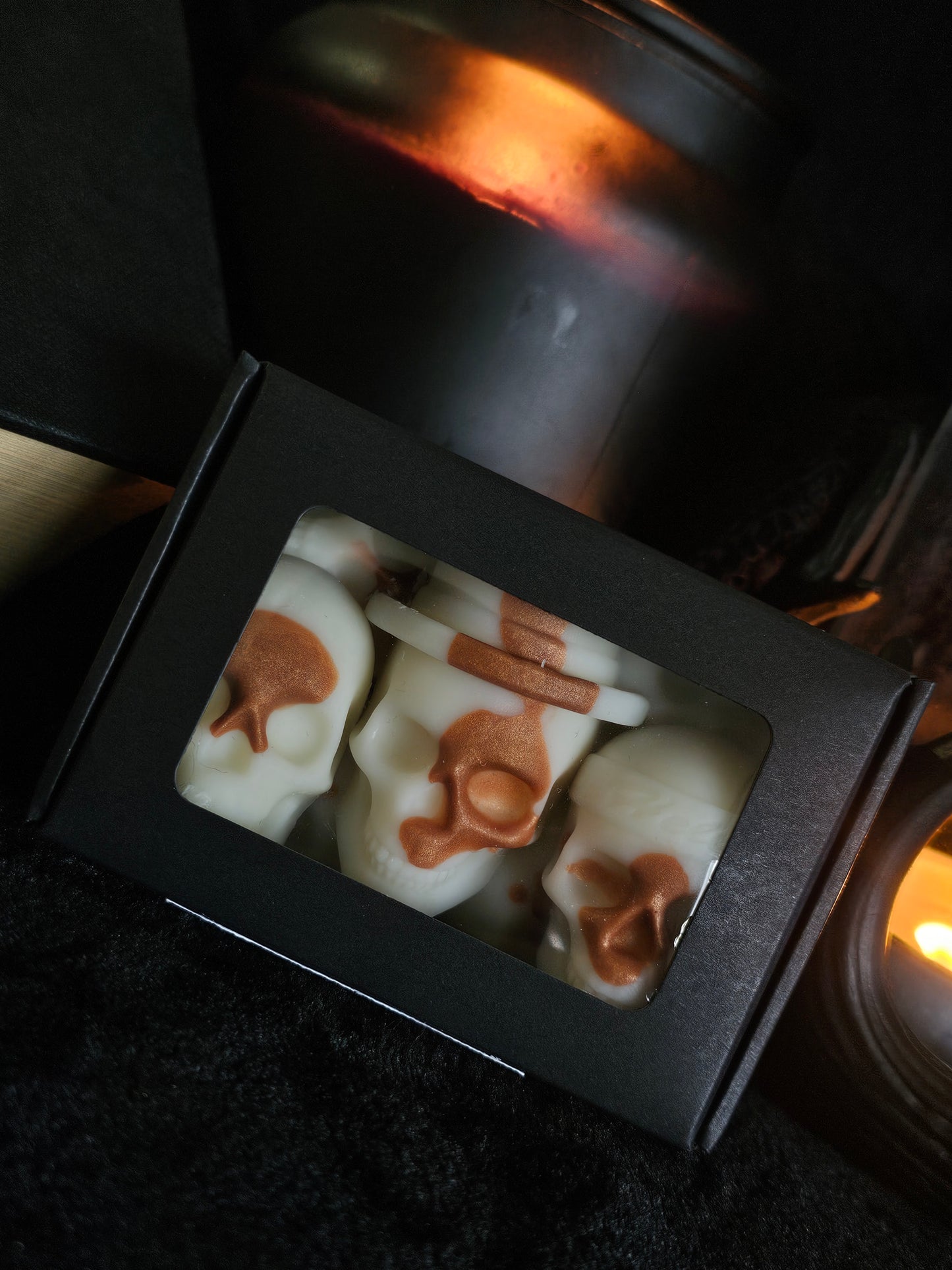 A box containing seven skull-shaped wax melts with a honeycomb pattern on the surface, displayed in a dark setting with candlelight.