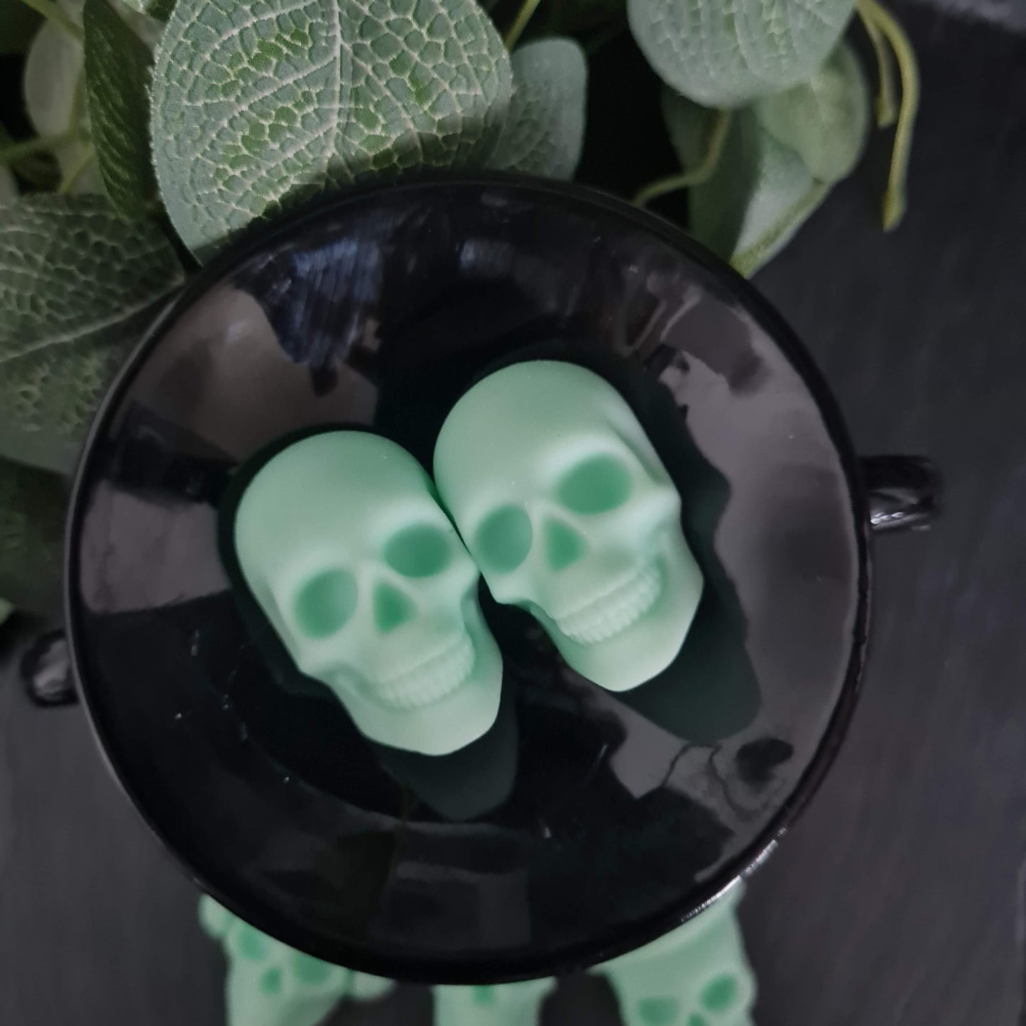 2 skull shaped wax melts in a cauldron on a dark surface 