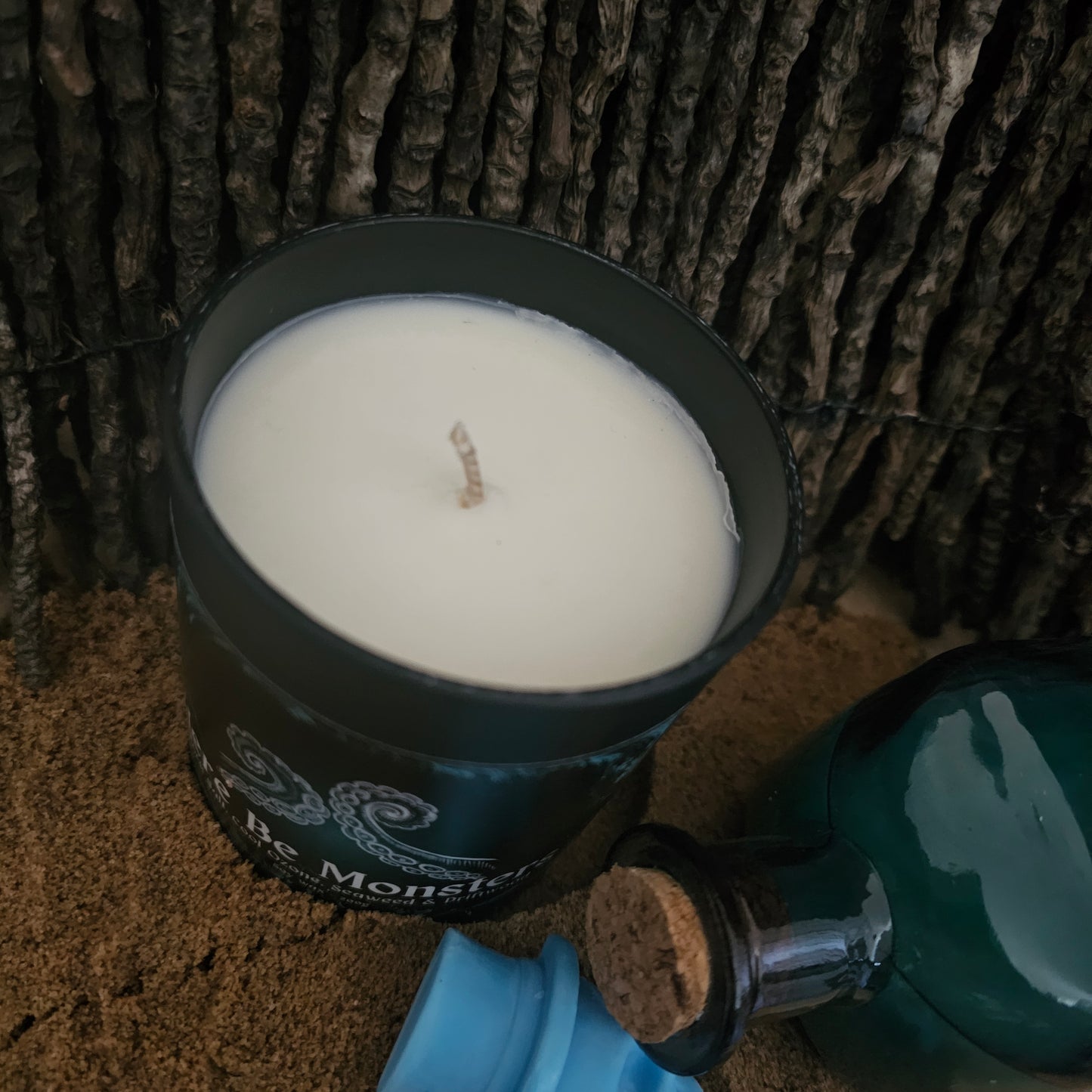 A top down angle of a candle in a black container on a sandy surface
