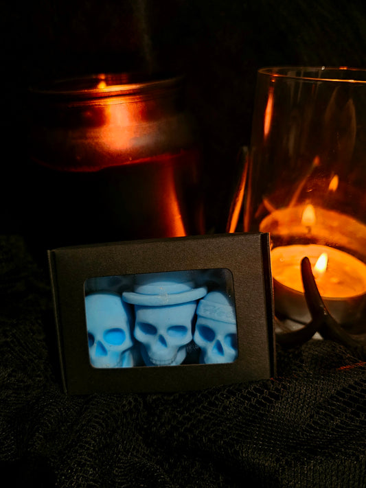 A box of blue skull-shaped wax melts with a candle in the background creating a warm glow.