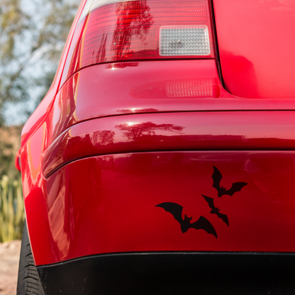 Black bat-shaped vinyl decals on the red rear bumper of a car.