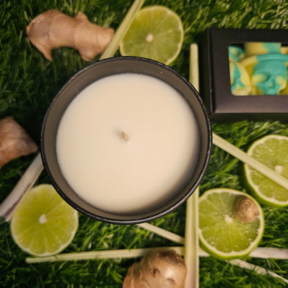 A candle veiwed from above, surrounded by lemongrass leaves, ginger roots, lime slices and yellow and green Skull shaped wax melts lay alogside the candle on a grassy background.