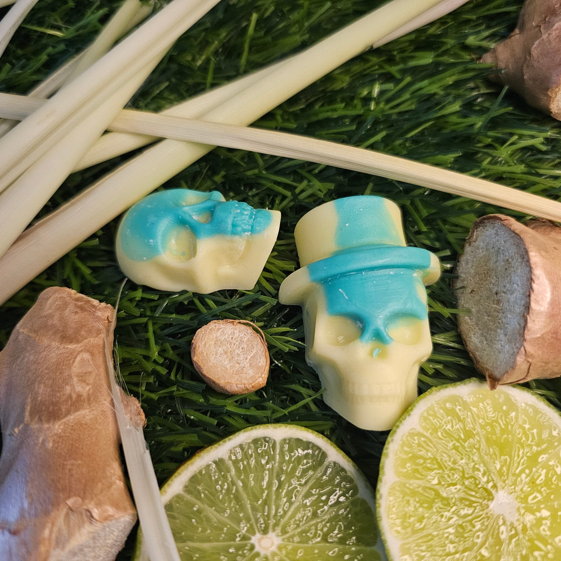 A skull-shaped wax melt, with a green and yellow design, surrounded by lime slices and ginger roots on a grassy background 