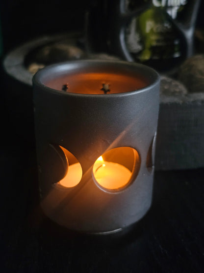 
Candle in a black ceramic holder with moon phases cut out.  on a dark background
