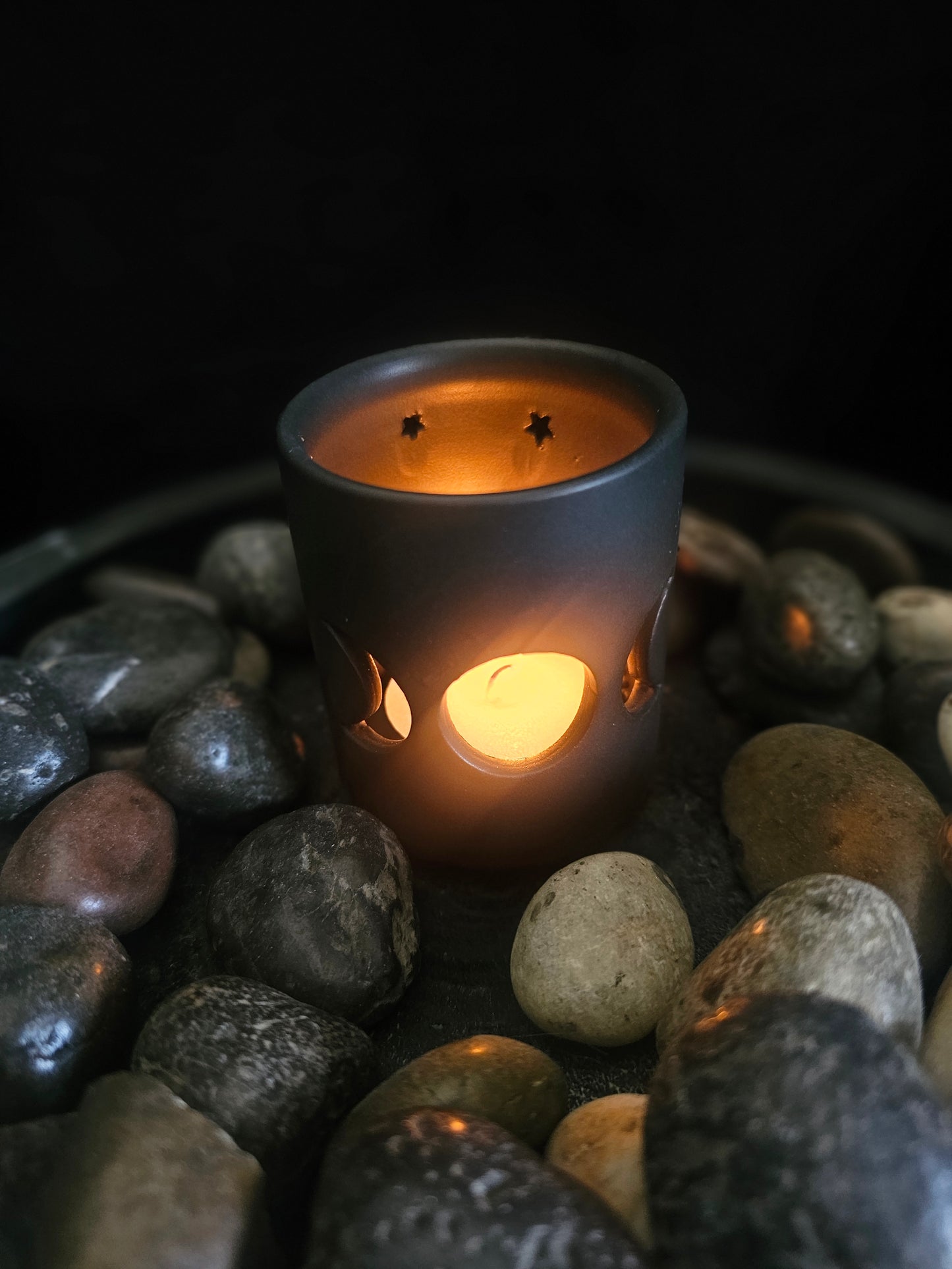 Candle holder with a lit candle on pebbles against a dark background