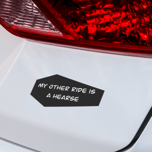 A black vinyl decal with the text 'MY OTHER RIDE IS A HEARSE' adhered to the rear of a white vehicle, near the tail light.