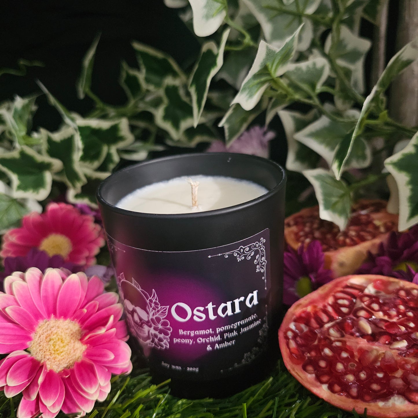 Candle in a Black container labeled Ostara surrounded by flowers and pomegranate slices 
