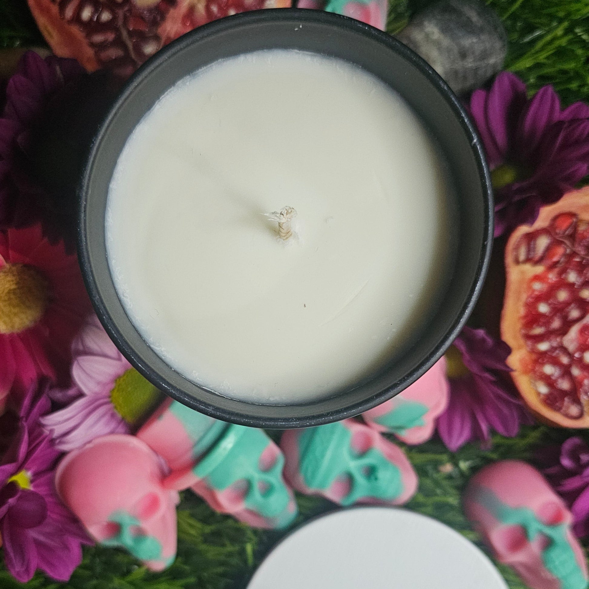 White candle in a black container surrounded by colorful flowers and decorative items
