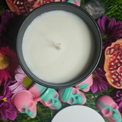 White candle in a black container surrounded by colorful flowers and decorative items
