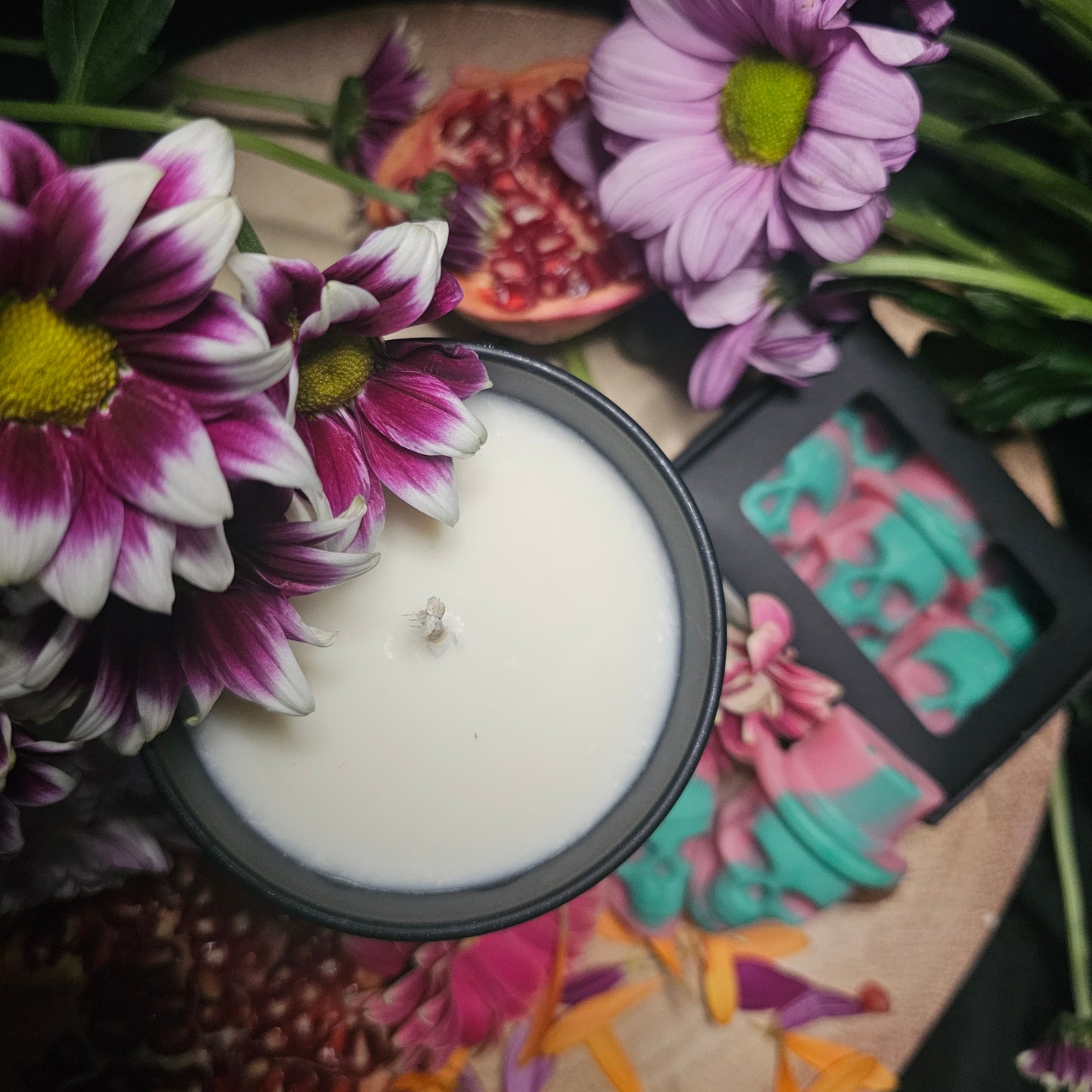 White candle in a black container surrounded by colorful flowers and skull shaped wax melts 