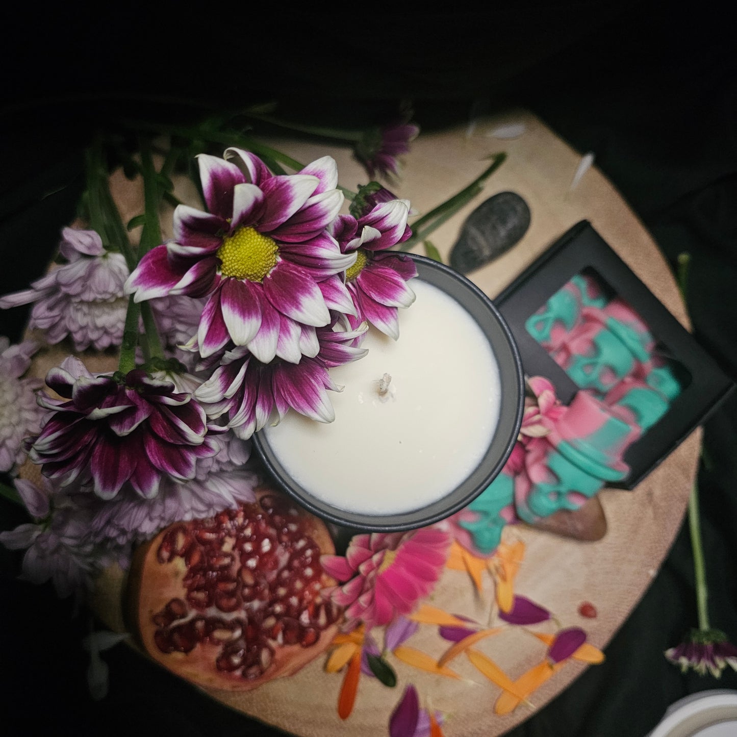 White candle in a black container surrounded by colorful flowers and skull shaped wax melts 