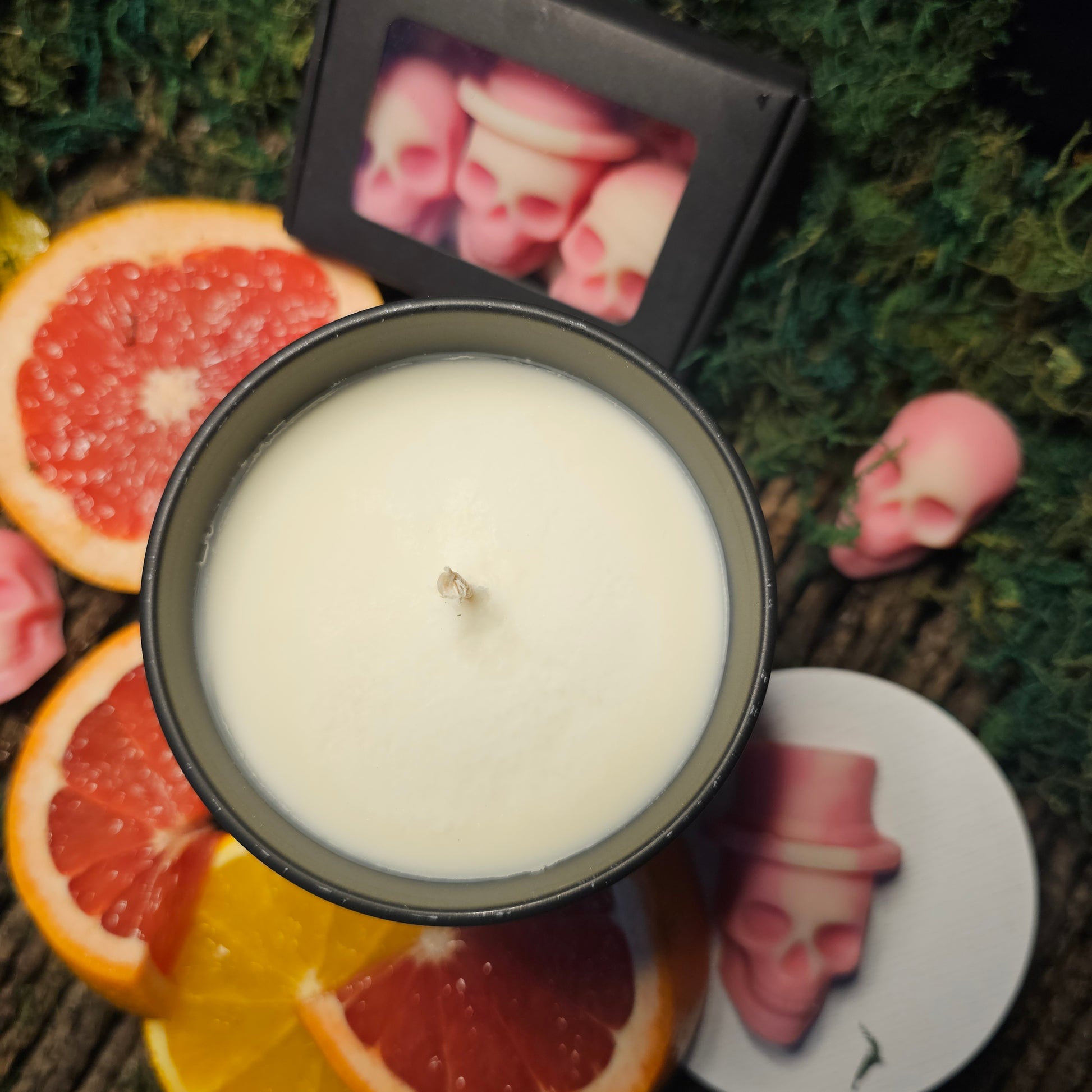 an overhead photograph showing the top of a cande housed in a black jar, surrounded by Bloodmoon wax melts and blood orange. 