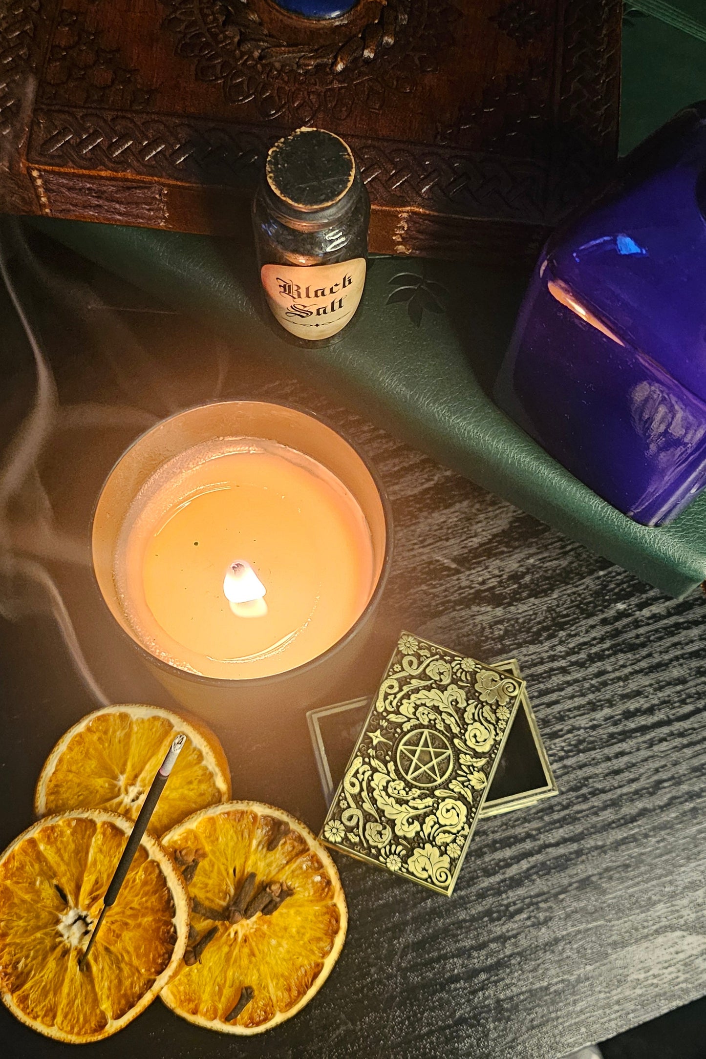 Lit candle surrounded by dried oranges, cloves, potion bottles and books 