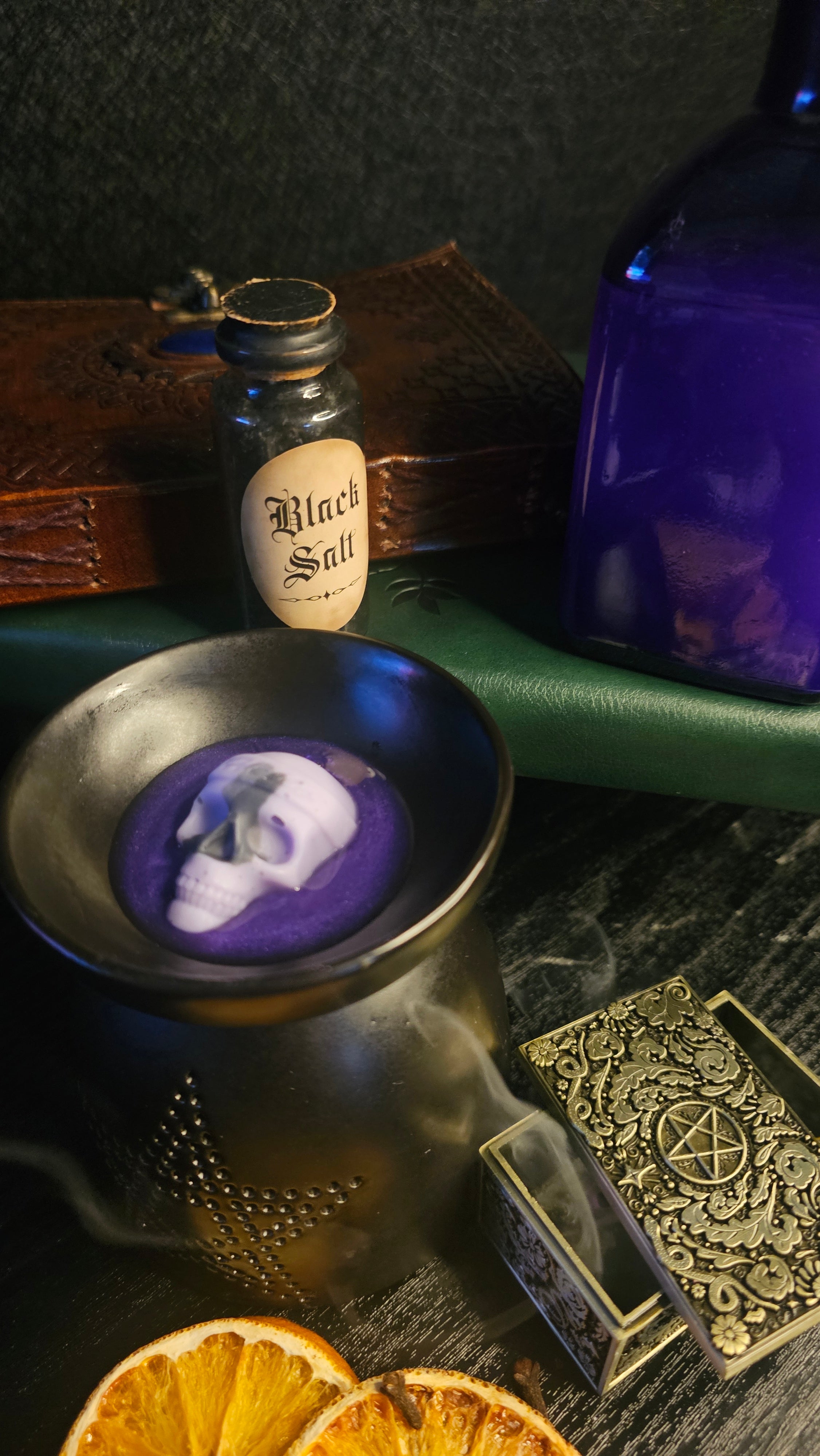 Wax melt with smoke, bottle, and dried oranges on a dark surface