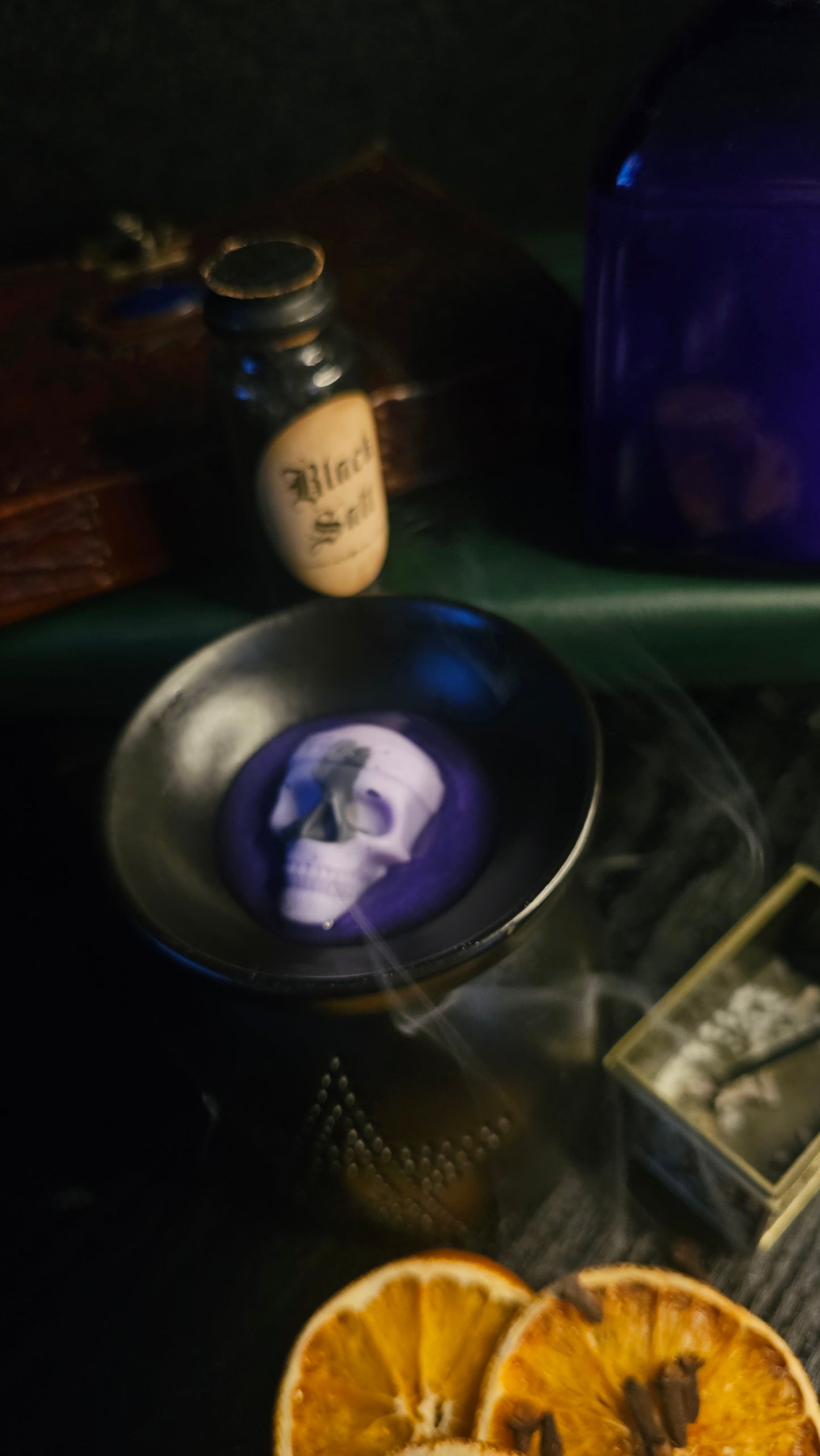 Wax melt with smoke, bottle, and dried oranges on a dark surface