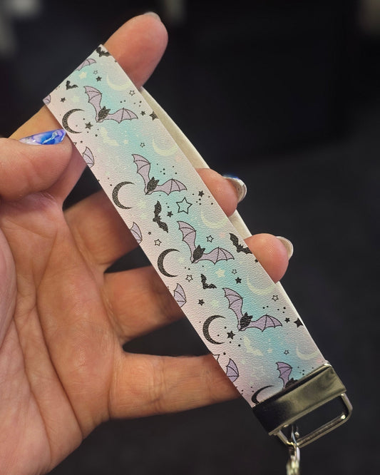 Keychain with a blush pink and powder blue pattern of bats, moons, and stars held in a hand against a dark background.