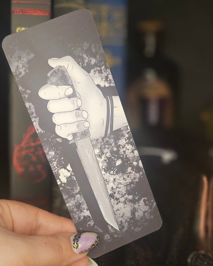 Bookmark with an illistration of a hand holding a knife held by a person against a blurred background