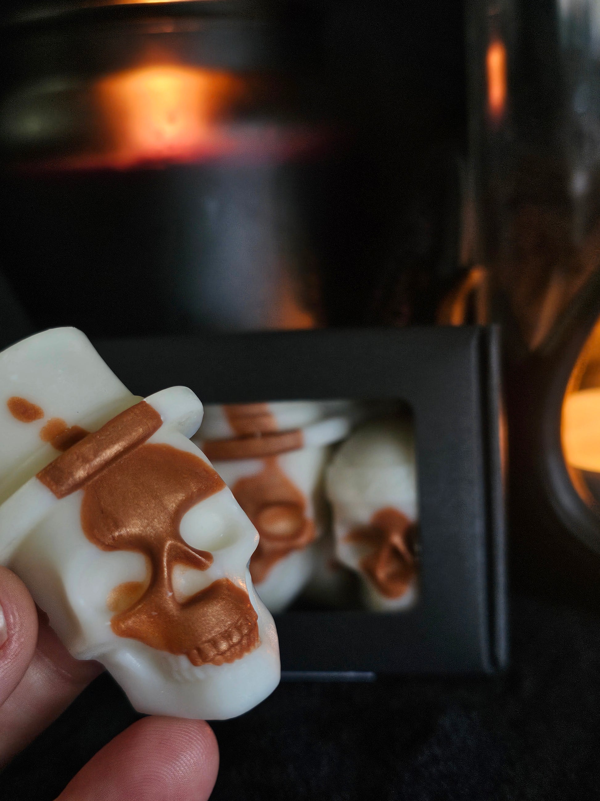 Nocturnal nectar skull wax melt held in a hand close up, with a candle and box of melts out of focus in the background 