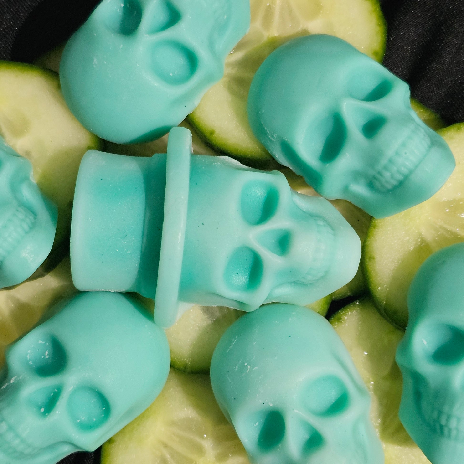 A collection of teal skull-shaped wax melts, arranged on a surface with cucumber slices.