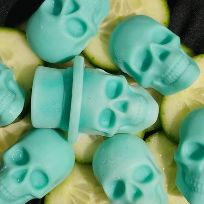 A collection of teal skull-shaped wax melts, arranged on a surface with cucumber slices.